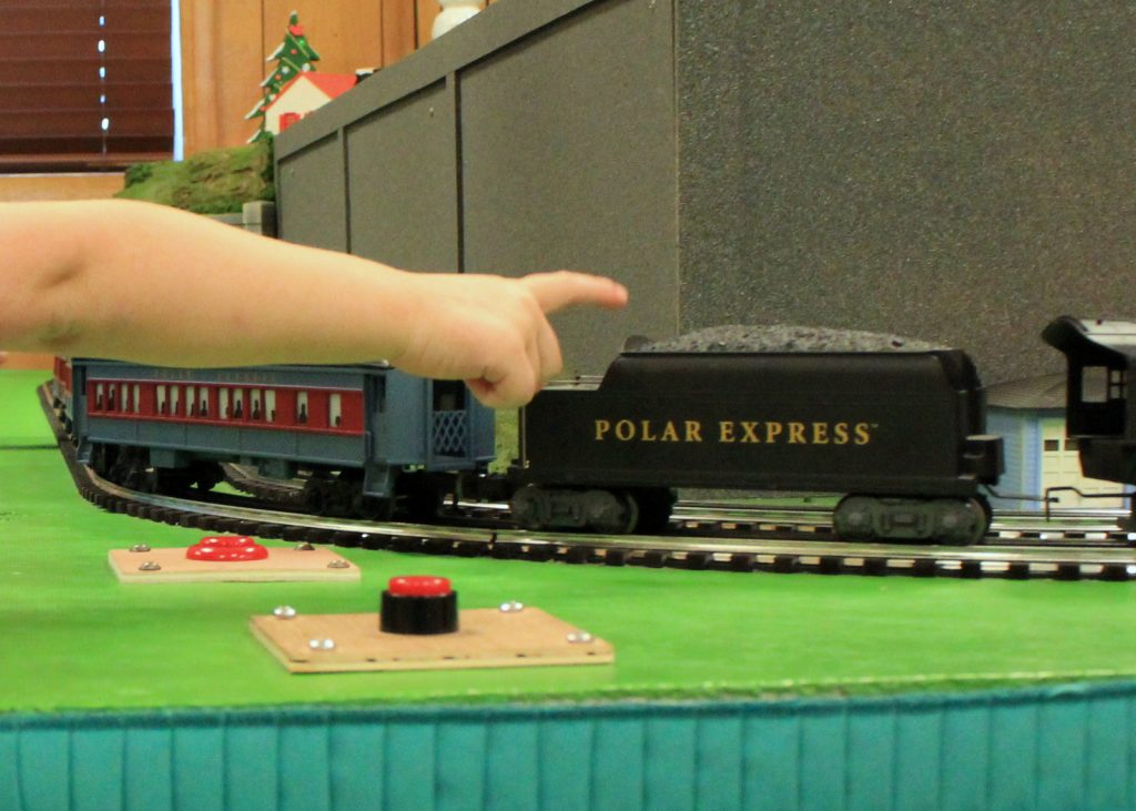 A child pointing to a model train cruising around tracks.