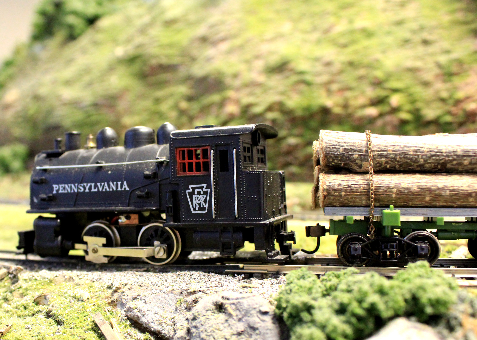 Model train engine pulling a car stacked with tree logs.