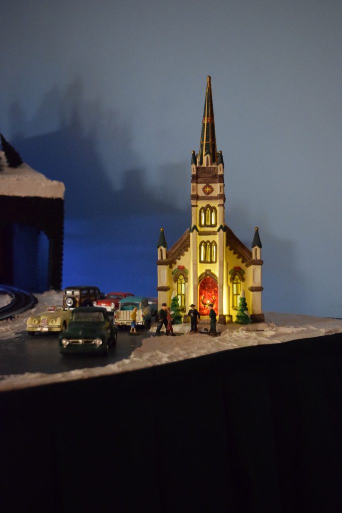 A winter scene, a church with a tall steeple, at night in town - Christmas at the Roundhouse" model train display.