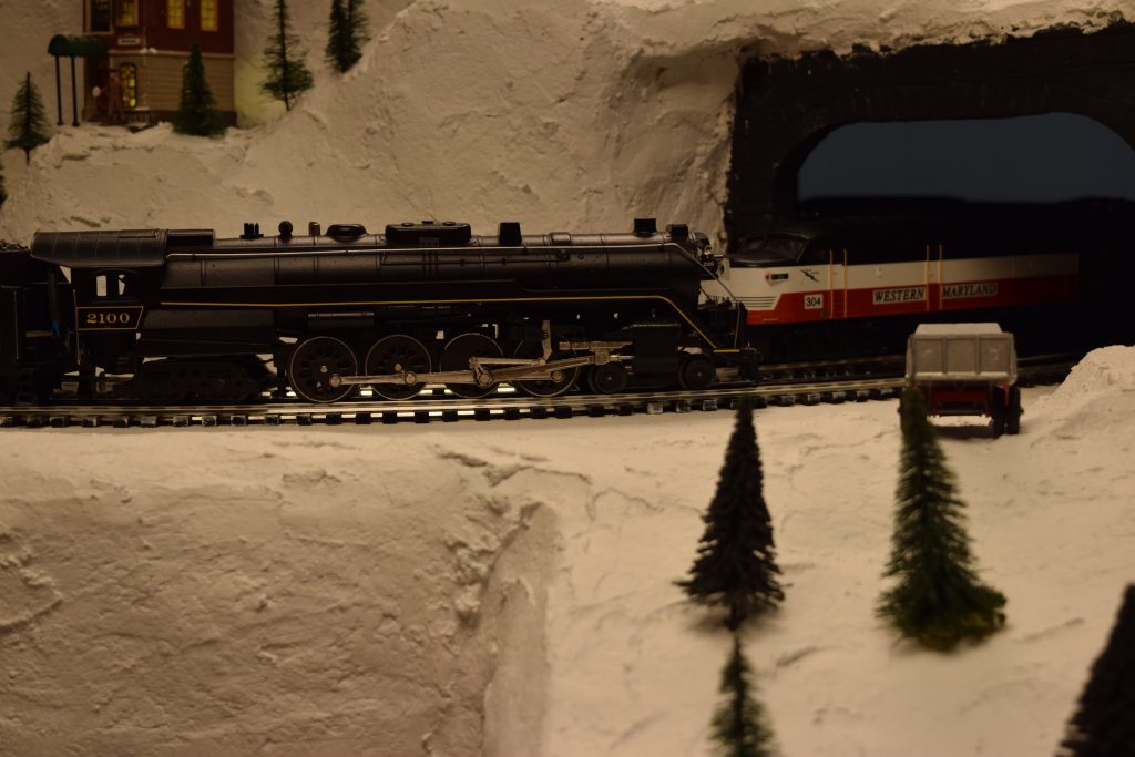 A mountain scene with a locomotive pulling freight cars on the mountain side - "Christmas at the Roundhouse" model train display.