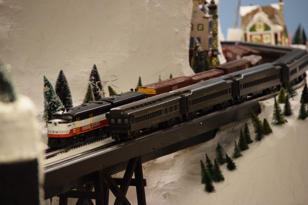 A snowy mountain scene with a two trains passing each other in opposite directions on the mountain side - "Christmas at the Roundhouse" model train display.