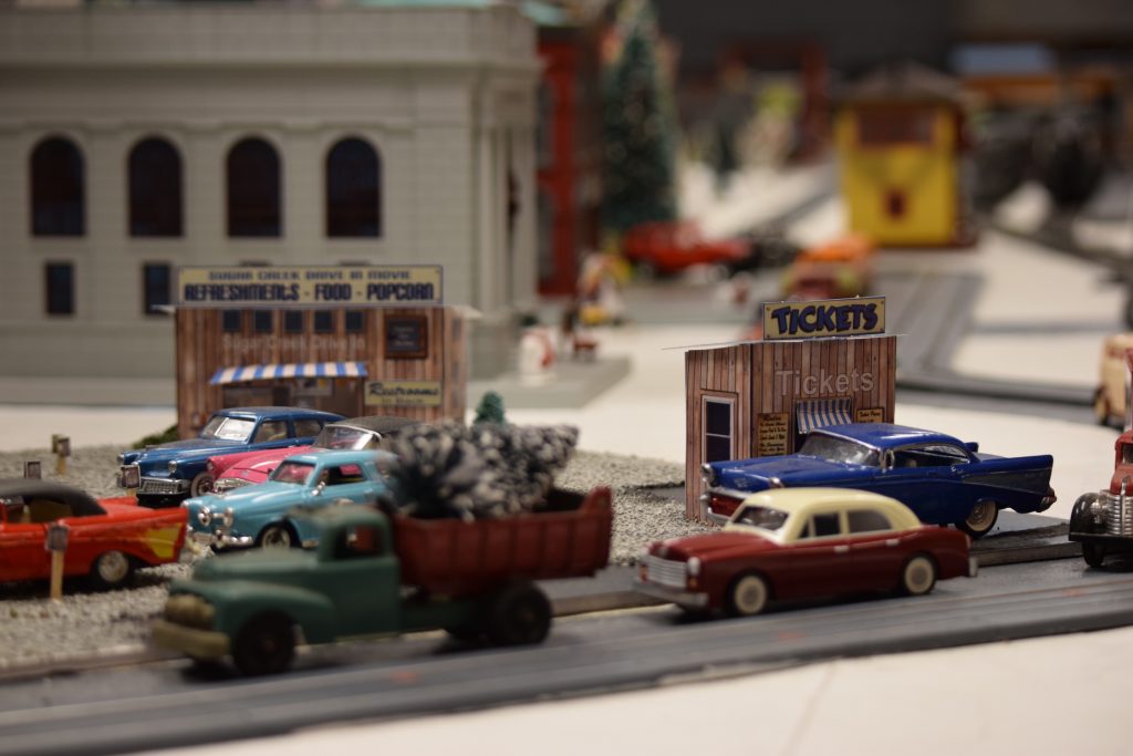 A drive-in movie scene with automobiles and a ticket booth - "Christmas at the Roundhouse" model train display.