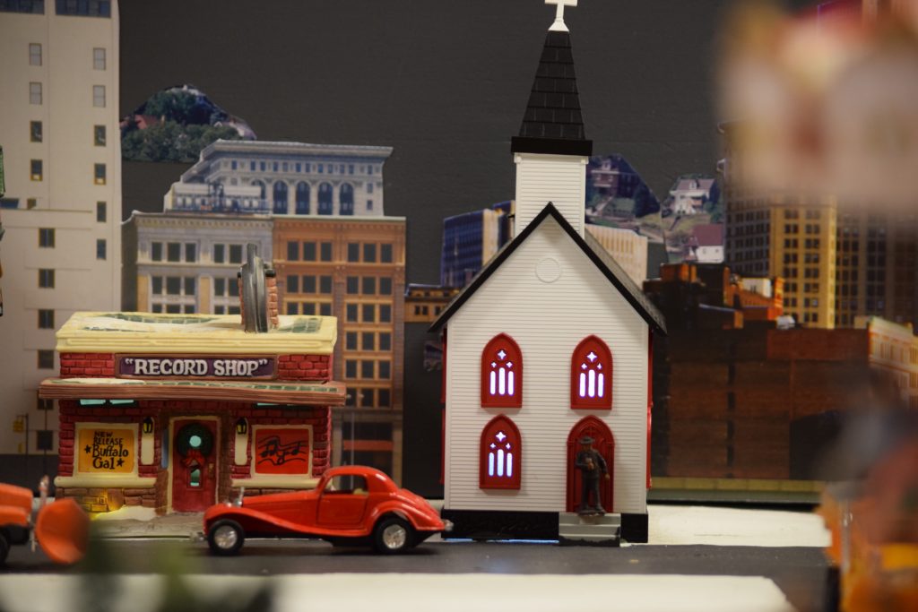 A vintage automobile parked in the street in front of a church in town - "Christmas at the Roundhouse" model train display.